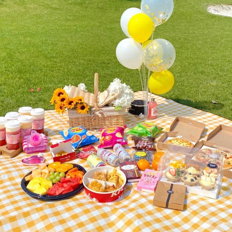 A picnic mat outside the field, with water and a thick, wild lawn and spring camp