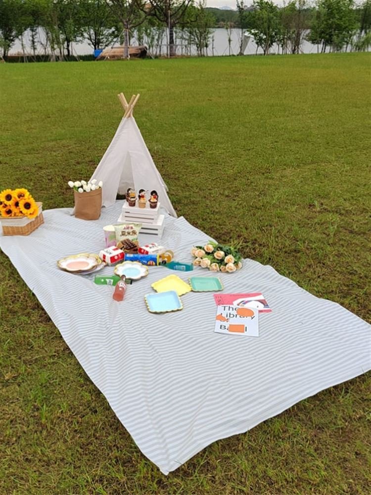 a striped picnic on a beach with a waterproof, sand-proof, open-sea-side camping pavilion with a tablecloth