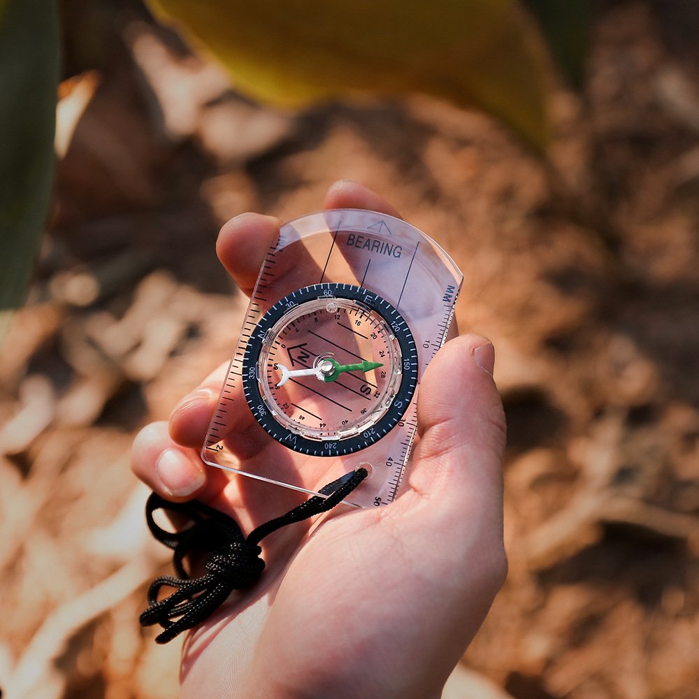 A professional multi-purpose compass for outdoor equipment in the wilderness points to a scale-scale compass of the north map