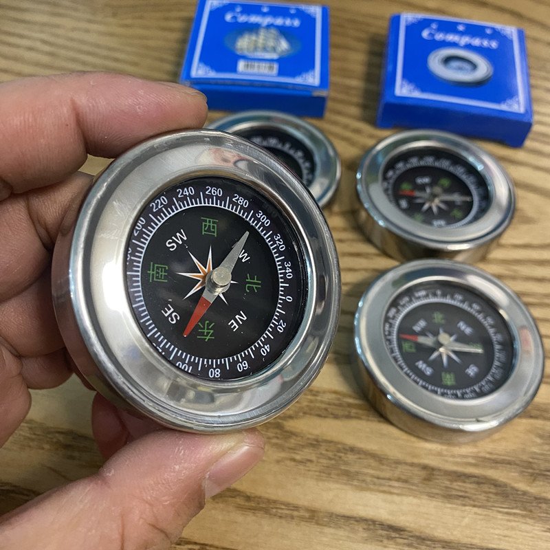 A compass, a metal shell, a hand-held metallic stainless steel pointer in an outdoor mountain trip