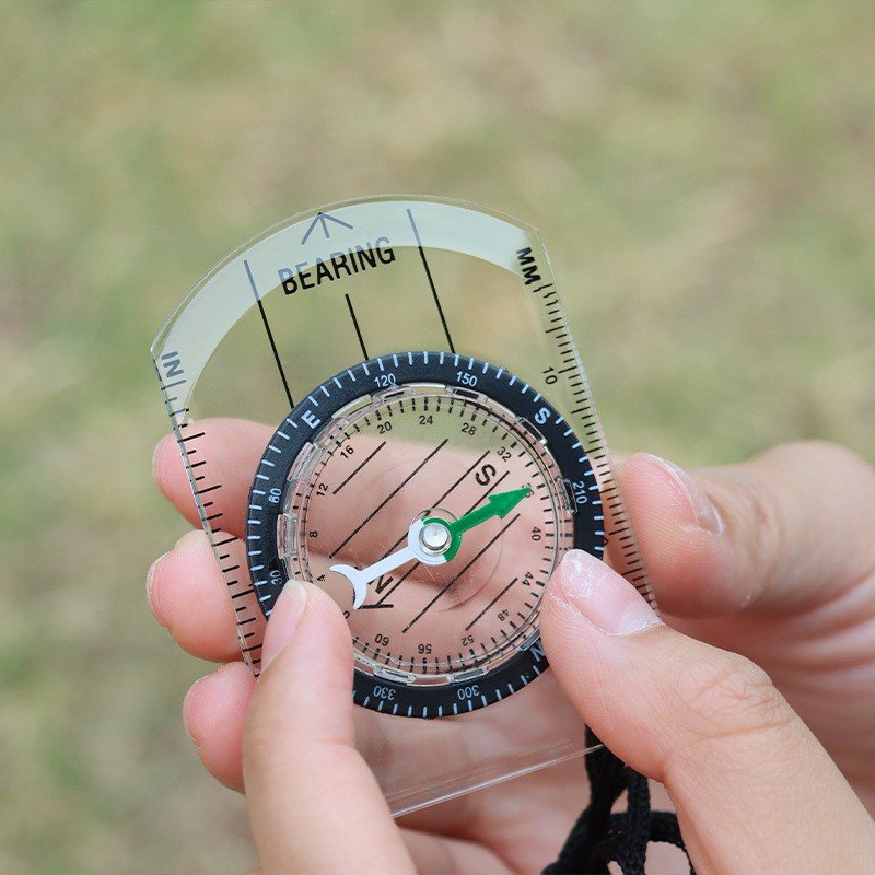 A professional multifunctional compass for survival in the wilderness points to the map of the outdoor equipment of the northern needle. A ruler compass