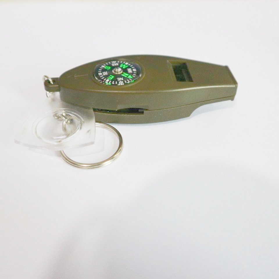 A multi-purpose whistle with a magnifying glass thermometer outside the perimeter of a four-point compass