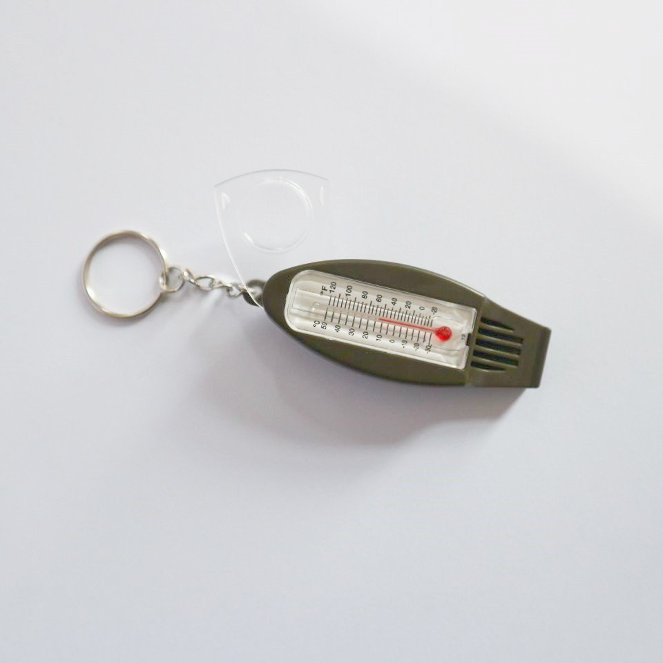 A multi-purpose whistle with a magnifying glass thermometer outside the perimeter of a four-point compass