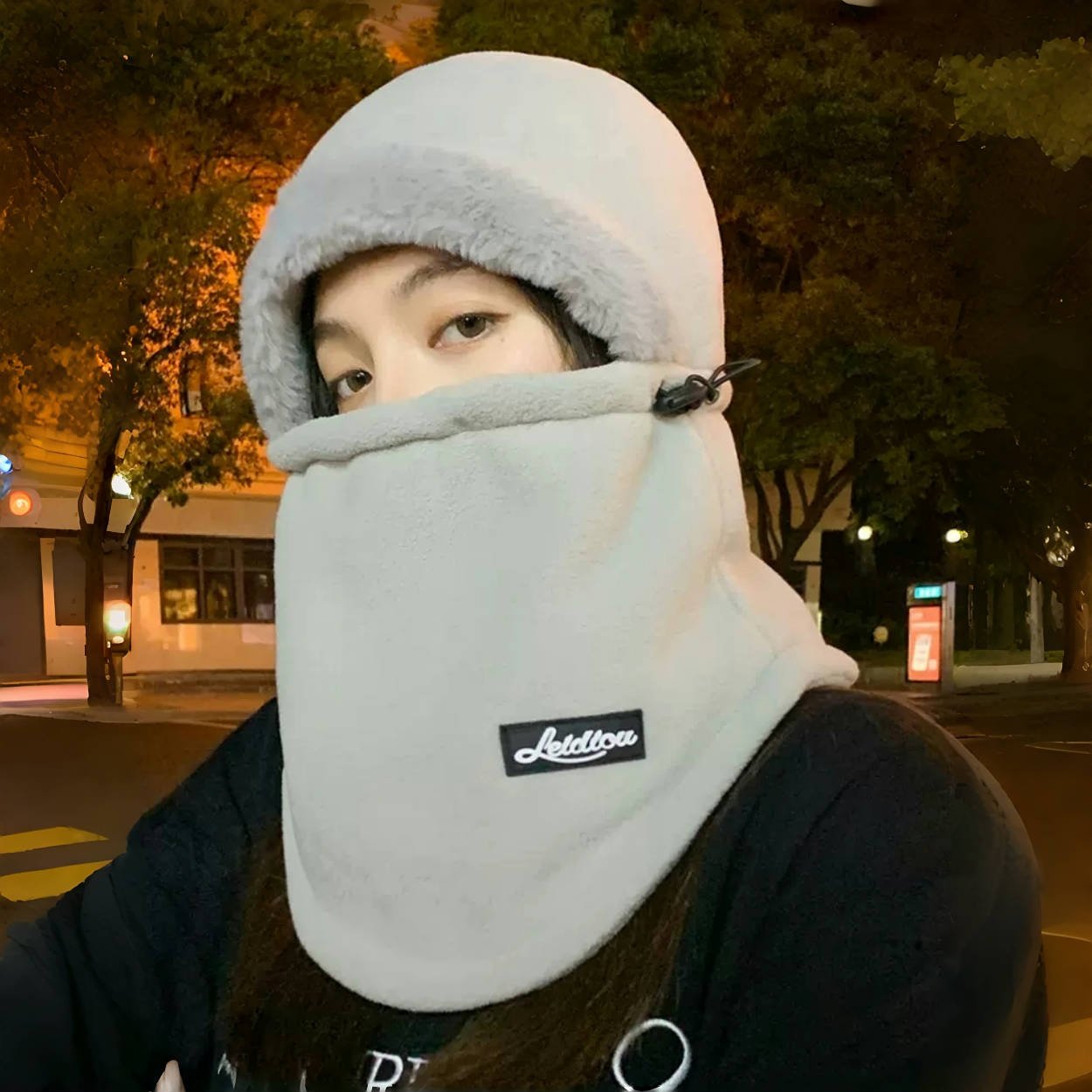 In winter, a woman with a warm head cap rides an electric car around with a decent ski mask and a cold neck scarf