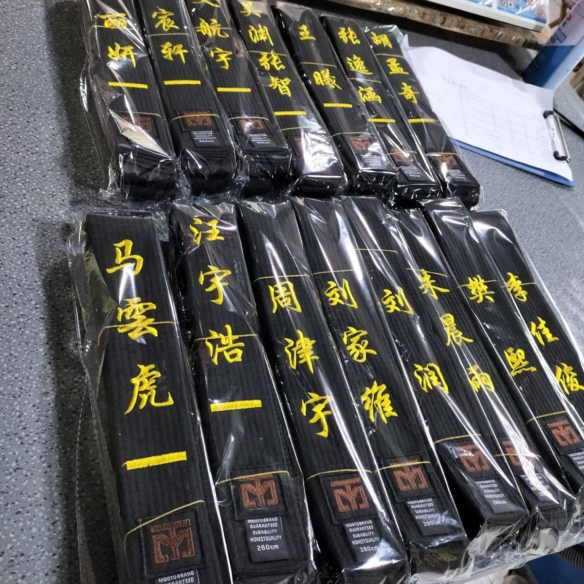 Taekwondo belts with children embroidered, black-banded athletes scattered with their coach's black-band karate belt